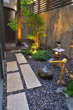 a small garden with rocks and gravel in the foreground is lit up by lights