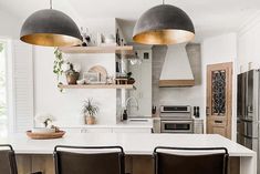 a kitchen with two pendant lights hanging over the island and three chairs in front of it