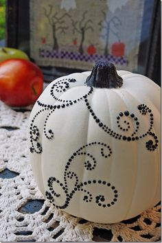 a white pumpkin decorated with black beading sits on a doily next to an apple