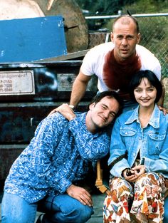 two men and a woman sitting on the back of a truck