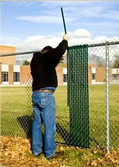 a man holding a baseball bat in front of a chain link fence with leaves on the ground