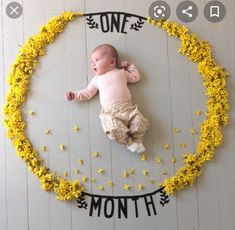 a baby laying on top of a wooden floor surrounded by yellow flowers and the words one month written above it