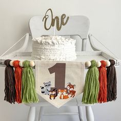 a one year old birthday banner with animals and tassels hanging from a chair