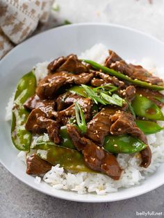 a white bowl filled with rice and beef on top of green peppers, as well as broccoli