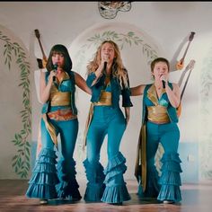 three women in blue and gold outfits singing into microphones