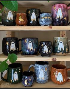 many different colored coffee mugs on shelves with plants in the corner and one has a ghost painted on it