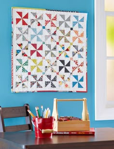 a room with a table, chair and quilt hanging on the wall