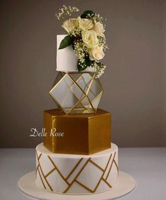 a three tiered white and gold wedding cake with flowers in the top, on a plate