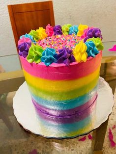 a rainbow cake with sprinkles and flowers on it sitting on a table