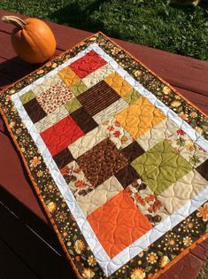 an orange pumpkin sitting on top of a wooden bench next to a patchwork quilt