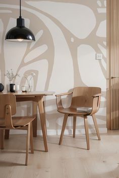 two wooden chairs sitting next to each other in front of a wall with an abstract design on it