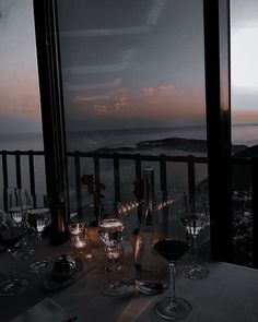 the table is set with wine glasses and plates on it, overlooking the ocean at dusk