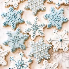 decorated cookies with blue frosting and snowflakes on top of a marble table