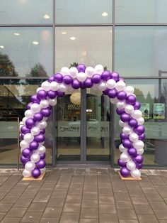 a purple and white balloon arch in front of a building