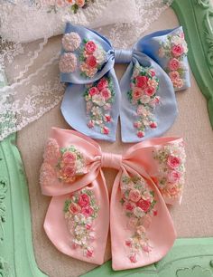 three bows with flowers on them are sitting on a table next to lace and fabric