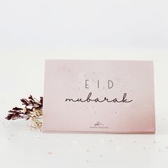 a card with the words eid mubarak written on it next to dried flowers