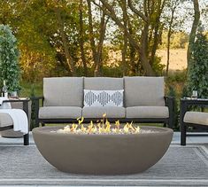 an outdoor fire pit sitting on top of a patio next to chairs and tables with pillows