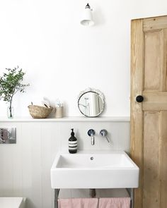 a white sink sitting under a bathroom mirror next to a wooden door and toilet paper dispenser