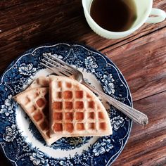 two waffles on a blue and white plate next to a cup of coffee