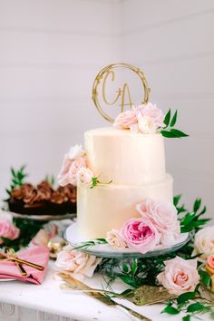 a three tiered cake with pink flowers and greenery sits on a white table