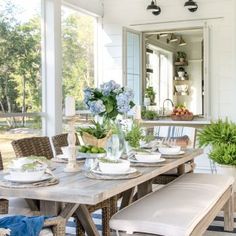 a dining room table set for four with blue flowers and greenery in the center