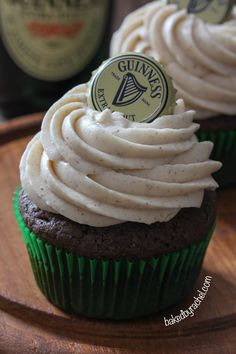 two cupcakes with white frosting on a wooden plate next to a bottle of guinness