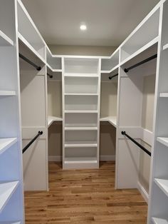 an empty walk in closet with white shelving and wood flooring on the side