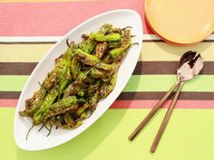 a white plate topped with green beans next to a yellow bowl and silver spoons