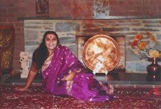 a woman in a purple sari sitting on the floor next to a fire place