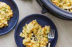 two blue plates with food on them next to a crock pot and silver fork