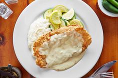 a white plate topped with fried chicken covered in gravy and cucumbers