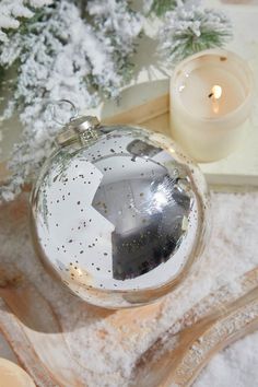 a christmas ornament sitting on top of a table next to candles and snow