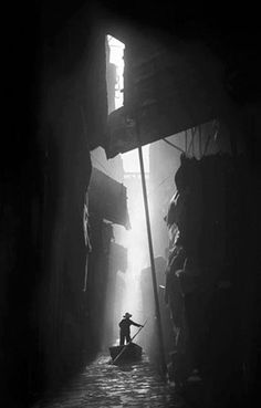 a black and white photo of a person on a boat in the dark alleyway