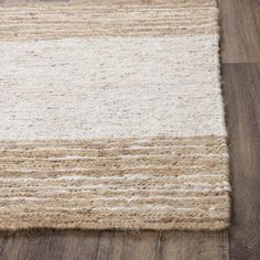 an area rug with white and beige stripes on the top, in front of a wooden floor