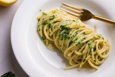 a white plate topped with pasta covered in sauce and parsley next to lemon wedges