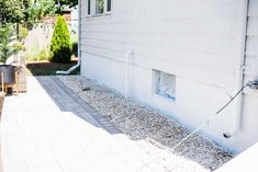 an outside view of a white house with gravel on the ground and plants in pots