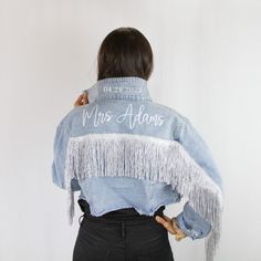 the back of a woman wearing a jean jacket with fringes and writing on it