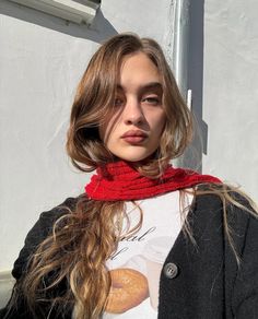 a woman with long hair wearing a black jacket and red scarf standing in front of a white building