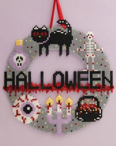 a cross stitch halloween ornament hanging from a red ribbon on a pink wall