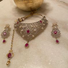 American Diamonds And Rubies Adorned Set Set In Art Like Design, In This Necklace, Earrings And Tika. Perfect For Any Formal Occasion To Glam Up Any Outfit. Designer Pink Wedding Sets, Designer Pink Jewelry For Formal Occasions, Elegant Red Bridal Sets With Stone Work, Pink Intricate Design Necklace For Wedding, Elegant Ruby Bridal Sets For Festive Occasion, Elegant Pink Necklace For Reception, Pink Wedding Necklaces With Intricate Design, Pink Fusion Jewelry For Formal Occasions, Elegant Pink Earrings For Reception