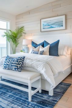 a large bed with blue and white pillows on top of it next to a window