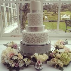 a wedding cake sitting on top of a table next to flowers and an open window