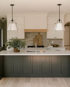 a large kitchen with white cabinets and gray island counter tops, along with two hanging lights over the sink