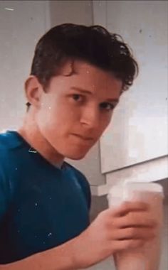 a young boy is holding a cup in his right hand and looking at the camera