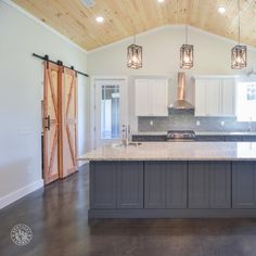 a large kitchen with an island in the middle and two lights hanging from the ceiling