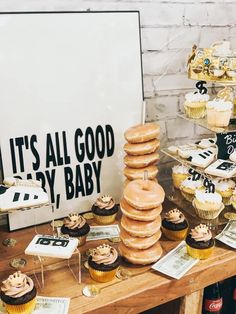 a table topped with lots of cupcakes next to a sign that says it's all good by baby