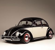 an old black and white beetle parked in front of a gray background with red rims