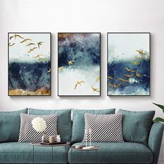 three paintings hang on the wall above a couch in a room with blue and white furniture