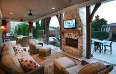 an outdoor living area with couches, chairs and a television on the fireplace in the center