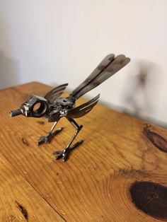 a small metal insect sitting on top of a wooden table next to a white wall